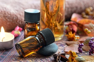 Bottles of essential oils on a decorative surface with a lit candle and dried flowers in the background.